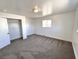 Unfurnished bedroom featuring baseboards, carpet flooring, a textured ceiling, and a closet
