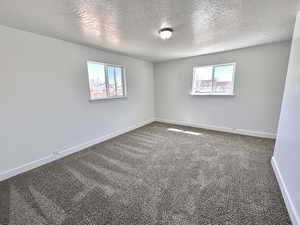 Carpeted spare room featuring a textured ceiling and baseboards