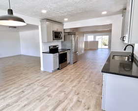 Kitchen featuring appliances with stainless steel finishes, a sink, open floor plan, light wood-style floors, and a textured ceiling