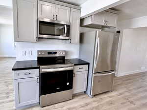 Kitchen with appliances with stainless steel finishes, light wood-type flooring, dark countertops, baseboards, and a textured ceiling