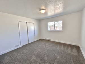 Unfurnished bedroom featuring a closet, dark carpet, baseboards, and a textured ceiling