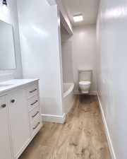 Full bathroom featuring wood finished floors, toilet, vanity, a tub, and baseboards
