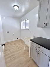 Laundry area featuring hookup for an electric dryer, washer hookup, light wood-style floors, a textured ceiling, and baseboards