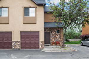 Townhome / multi-family property with stone siding, a shingled roof, stucco siding, and a garage