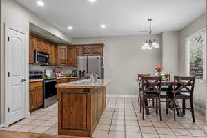 Kitchen featuring appliances with stainless steel finishes, a sink, baseboards, an island with sink, and recessed lighting