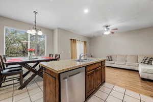 Kitchen featuring stainless steel dishwasher, a sink, open floor plan, light countertops, and light tile patterned floors