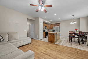 Living area with a chandelier, ceiling fan, recessed lighting, light wood-style floors, and baseboards