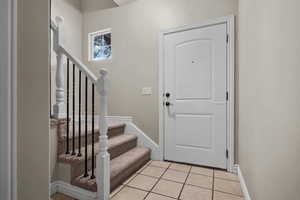 Entryway featuring baseboards, light tile patterned floors, and stairway