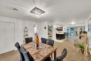 Dining area featuring light colored carpet, a chandelier, and a textured ceiling