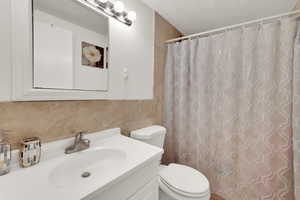 Full bathroom with toilet, vanity, decorative backsplash, and curtained shower