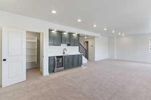 Indoor wet bar with beverage cooler, light colored carpet, baseboards, recessed lighting, and stairs