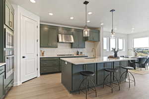 Kitchen featuring pendant lighting, a breakfast bar area, green cabinets, backsplash, and light wood-style flooring