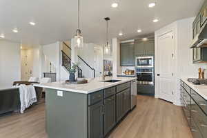 Kitchen with green cabinetry, light wood-style flooring, pendant lighting, an island with sink, and recessed lighting