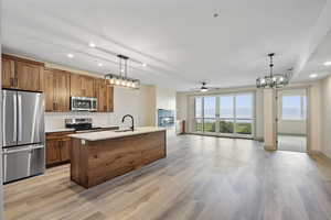 Kitchen with recessed lighting, brown cabinetry, stainless steel appliances, open floor plan, and decorative light fixtures