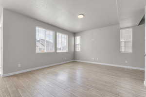 Unfurnished room featuring a textured ceiling, light wood-style flooring, plenty of natural light, and baseboards