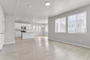 Unfurnished living room with a chandelier, baseboards, light wood finished floors, recessed lighting, and a textured ceiling