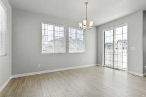 Unfurnished room with a chandelier, wood finished floors, and baseboards