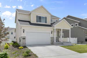 View of front of home featuring covered porch, driveway, roof with shingles, and stone siding
