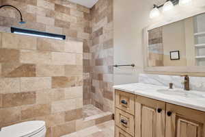 Bathroom with tiled shower, vanity, and toilet
