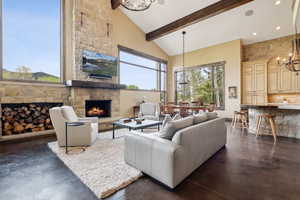 Living room featuring a chandelier, a fireplace, high vaulted ceiling, beam ceiling, and concrete floors