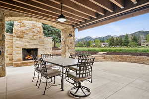 View of patio / terrace featuring an outdoor stone fireplace, a mountain view, a ceiling fan, and outdoor dining area