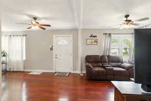 Living area featuring a ceiling fan, dark wood-type flooring, baseboards, and a textured ceiling