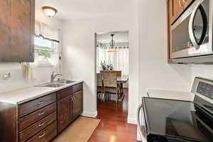 Kitchen featuring stainless steel appliances, a sink, dark wood-style flooring, light countertops, and dark brown cabinetry