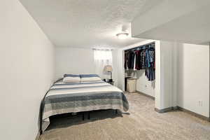 Bedroom featuring a textured ceiling, baseboards, light carpet, and a closet