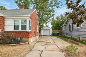 View of side of property featuring brick siding, concrete driveway, a detached garage, and a chimney