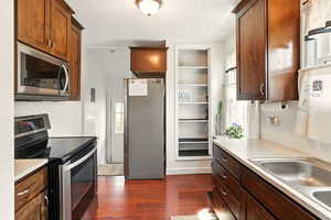 Kitchen featuring appliances with stainless steel finishes, a sink, dark wood-type flooring, and light countertops
