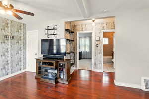 Living room featuring a ceiling fan, baseboards, a textured ceiling, wood finished floors, and wooden walls