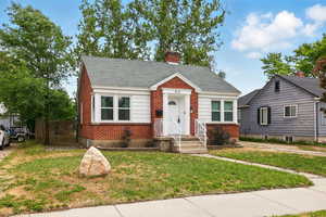 Bungalow-style house featuring brick siding, a front lawn, a chimney, and roof with shingles