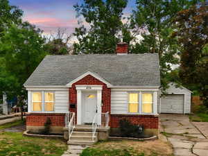 View of front facade featuring a chimney, concrete driveway, brick siding, and a lawn