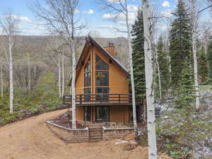 View of front of property featuring a chimney, a wooden deck, and a view of trees