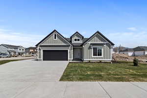 View of front facade featuring board and batten siding, concrete driveway, a front yard, and an attached garage