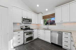 Kitchen with stainless steel appliances, a sink, vaulted ceiling, white cabinetry, and decorative backsplash