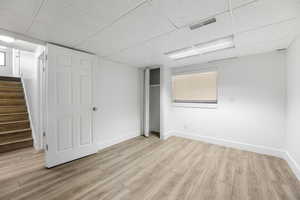 Finished basement with a paneled ceiling, light wood-style flooring, stairway, and baseboards