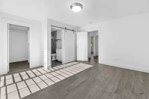 Unfurnished bedroom featuring baseboards, wood finished floors, a walk in closet, a barn door, and a closet