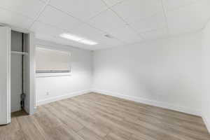 Unfurnished bedroom with a paneled ceiling, light wood-type flooring, and baseboards