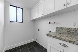 Laundry room with electric dryer hookup, cabinet space, baseboards, and dark tile patterned floors
