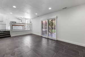 Spare room featuring a textured ceiling, plenty of natural light, recessed lighting, baseboards, and dark tile patterned floors