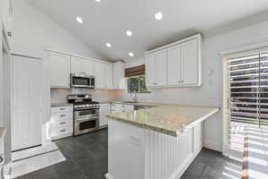 Kitchen featuring appliances with stainless steel finishes, a sink, a peninsula, lofted ceiling, and white cabinets