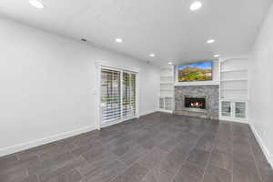 Unfurnished living room with a textured ceiling, baseboards, recessed lighting, a glass covered fireplace, and built in shelves