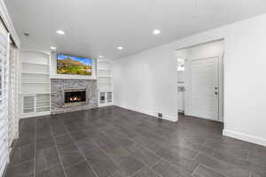 Unfurnished living room featuring a fireplace, a textured ceiling, built in shelves, baseboards, and recessed lighting