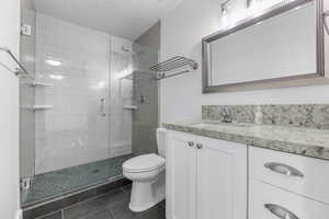 Full bathroom featuring toilet, a stall shower, a textured ceiling, vanity, and tile patterned flooring