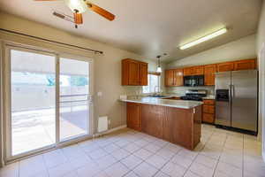 Kitchen with stainless steel refrigerator with ice dispenser, black microwave, gas range oven, brown cabinetry, and a sink