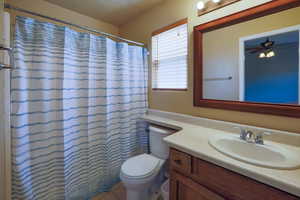 Bathroom with toilet, vanity, ceiling fan, and a shower with shower curtain