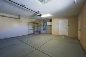 Garage with strapped water heater, a garage door opener, and baseboards
