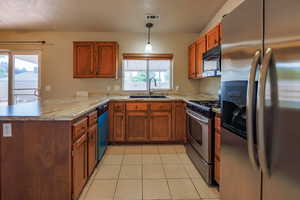 Kitchen with stainless steel appliances, a sink, a peninsula, brown cabinetry, and light tile patterned flooring