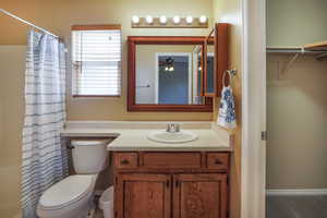 Bathroom with toilet, curtained shower, vanity, and ceiling fan